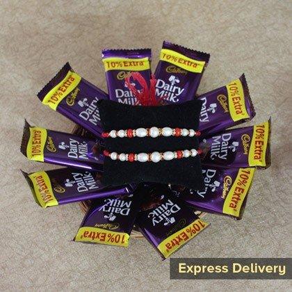 Rakhi set with red and white beads, surrounded by Dairy Milk chocolate bars, express delivery