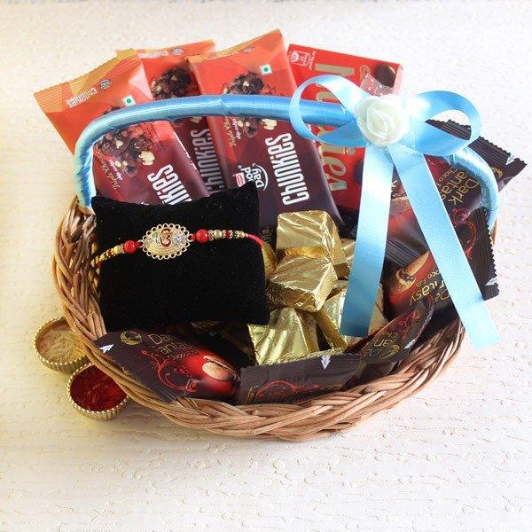 Rakhi gift basket with chocolates, a decorative rakhi, sweets, and blue ribbon handle.