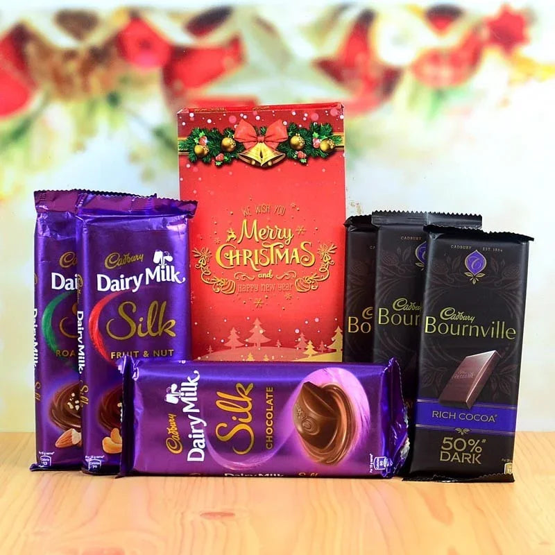 Assorted Cadbury chocolate bars and a Christmas-themed box on a wooden surface.