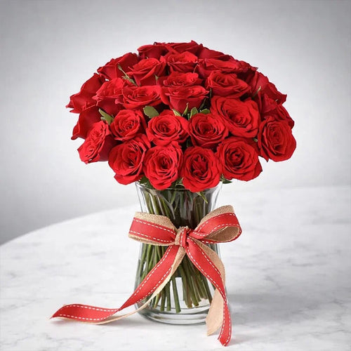 Bouquet of red roses in a clear vase with a red ribbon on a white background