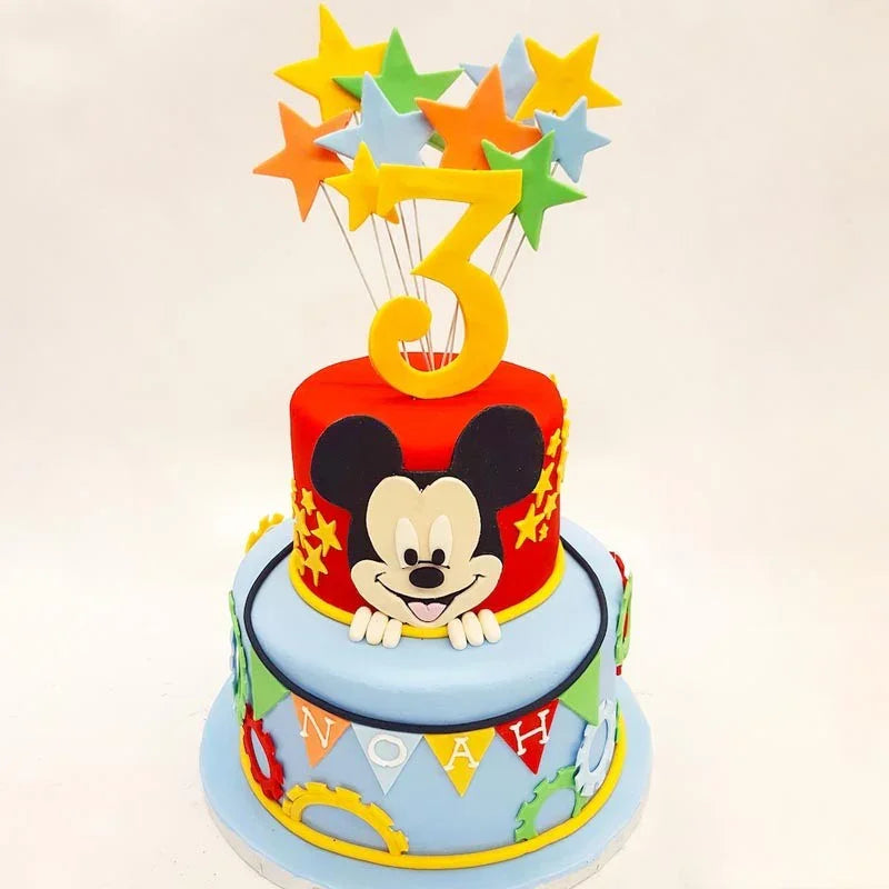 Two-tiered birthday cake with Mickey Mouse design and colorful star topper on a white background