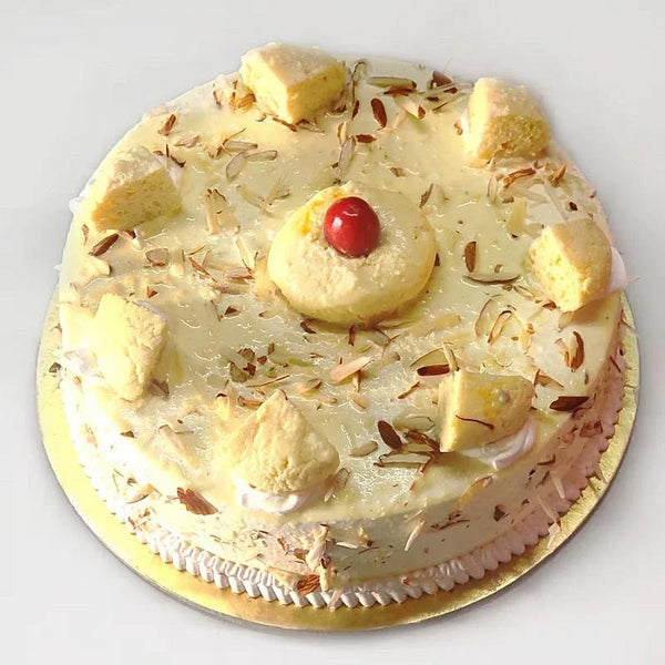 Decorative cake with nuts and a cherry on top, placed on a white surface.