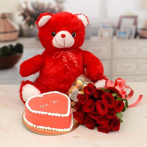 Red teddy bear with a heart-shaped cake and bouquet of red roses on a table.