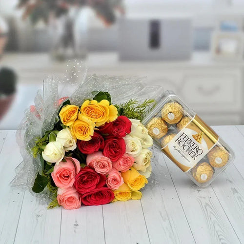 Bouquet of multicolored roses and a box of Ferrero Rocher chocolates on a light wooden surface.