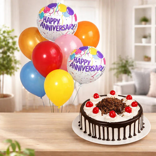 Anniversary cake with chocolate drizzle and cherries, accompanied by colorful 'Happy Anniversary' balloons on a wooden table.