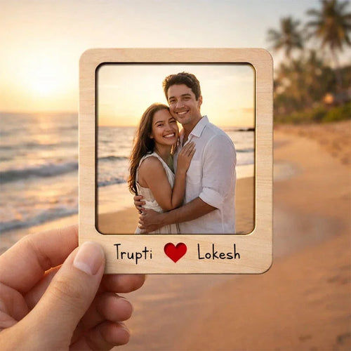 Wooden photo frame with a couple on a beach at sunset, held by a hand.