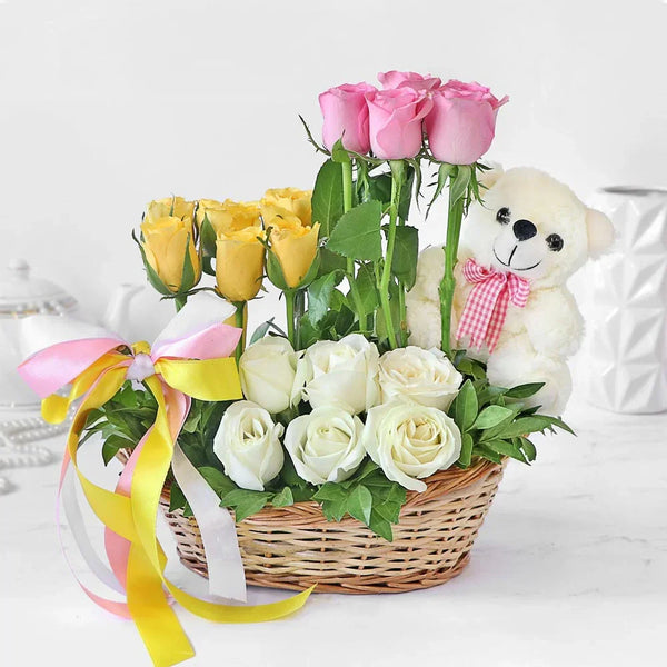 Basket with pink, yellow, and white roses, teddy bear, and colorful ribbon, gift arrangement