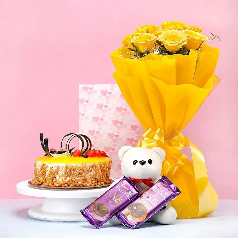 Bouquet of yellow roses, cake, teddy bear, and chocolate bars on a pink background