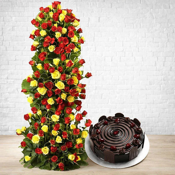 Tower of red and yellow roses with a round chocolate cake on a wooden table