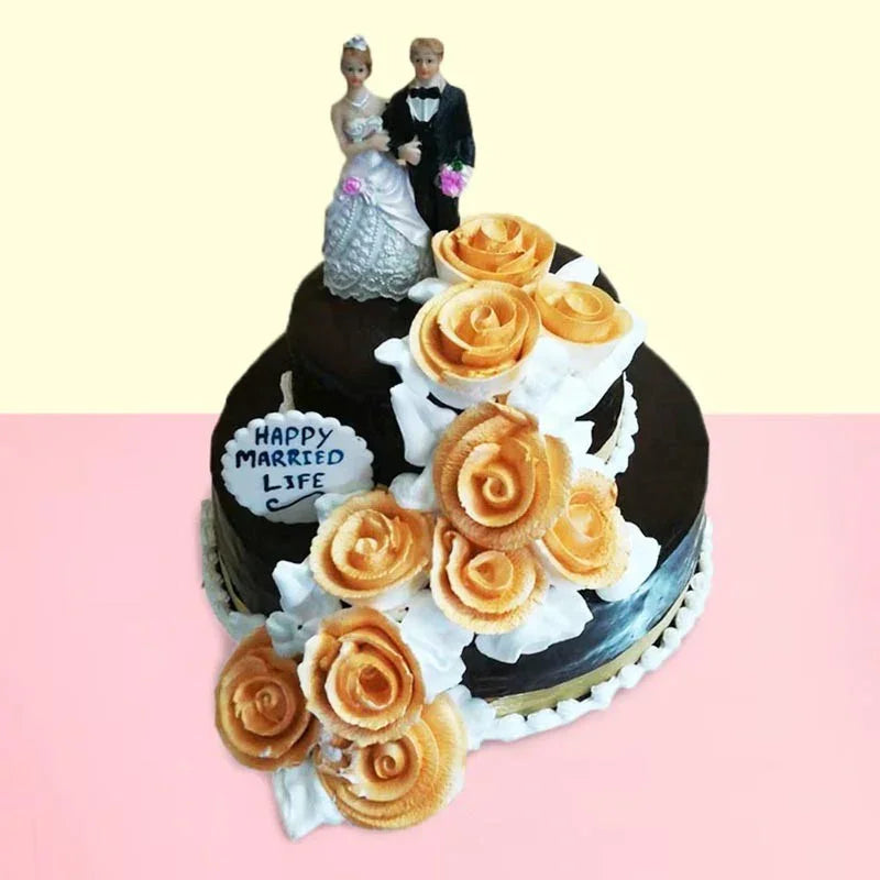 Wedding cake with floral decorations and bride and groom figurines on a pink and yellow gradient background.