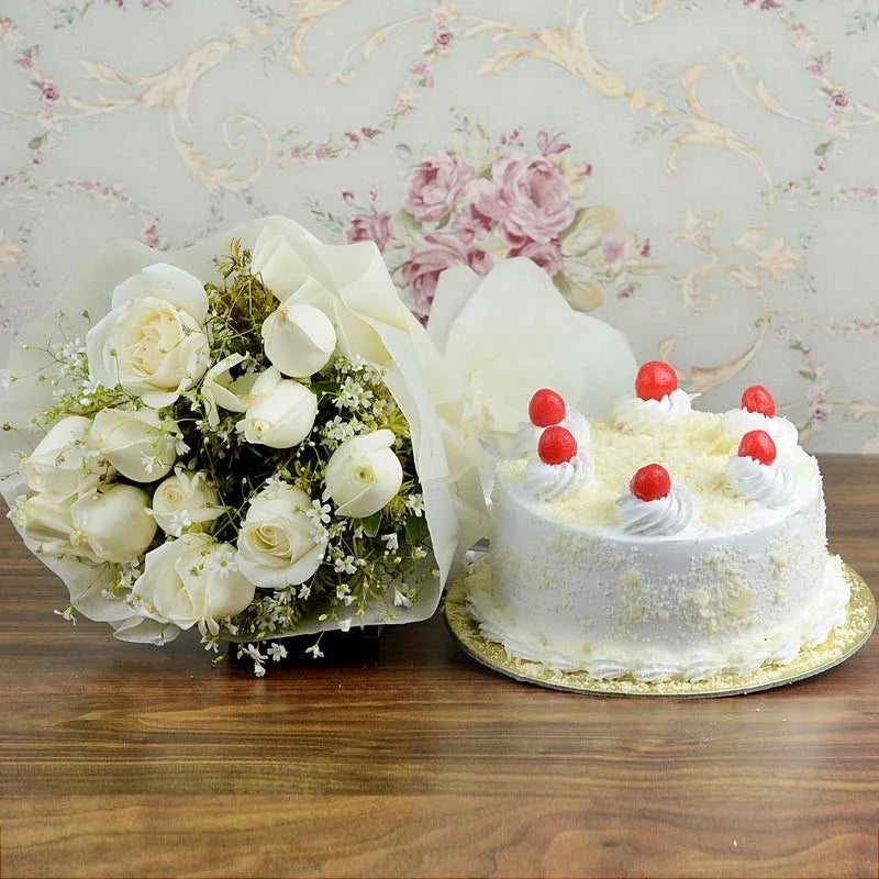 Bouquet of white roses and a small white cake with red decorations on a wooden table.