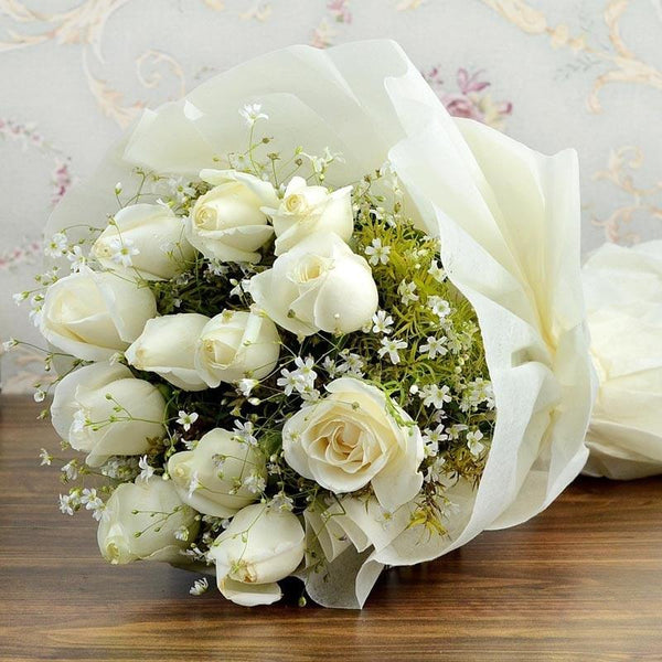 Bouquet of white roses with greenery on a wooden surface