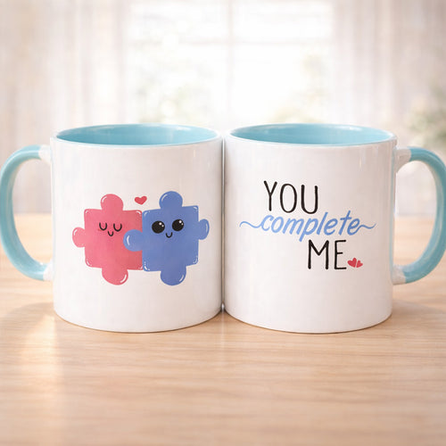 Two mugs with a design of two colorful characters and the text 'You complete me' on a wooden surface.