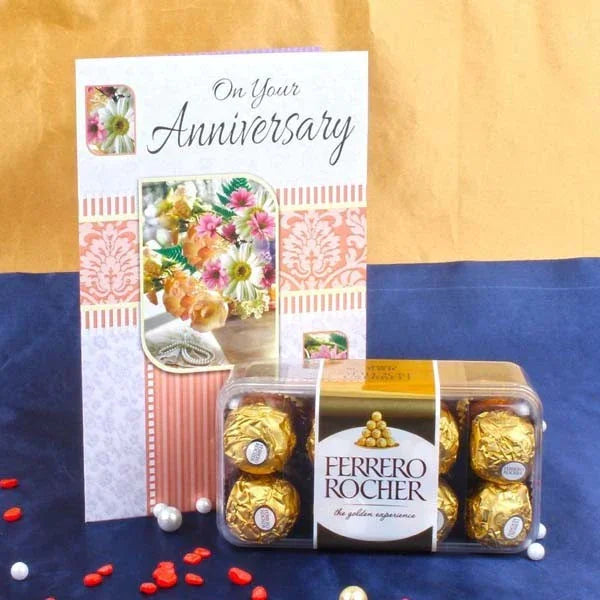 Ferrero Rocher chocolate box with an 'On Your Anniversary' card on a blue and gold fabric background.