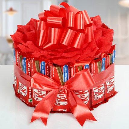 Red-wrapped candy bar gift tower with a large bow on a white surface.