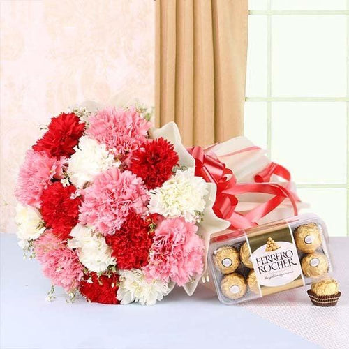 Bouquet of red, pink, and white flowers with a box of Ferrero Rocher chocolates on a light background.