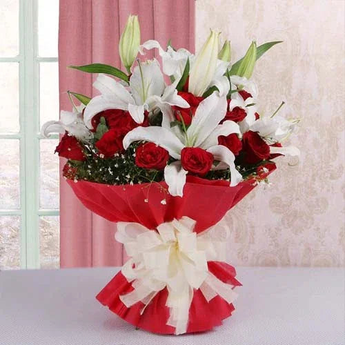 Bouquet of red roses and white lilies wrapped in red paper with a large white bow.