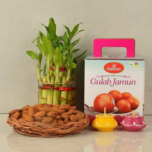 Gift set with lucky bamboo plant, Haldiram’s Gulab Jamun box, almonds in basket, and decorative diyas