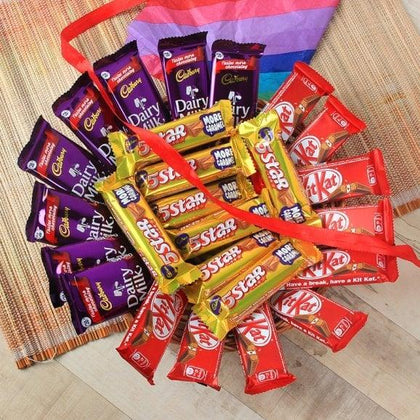 Gift arrangement of Dairy Milk, 5 Star, and KitKat chocolates with red ribbon on mat