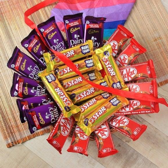 Gift arrangement of Dairy Milk, 5 Star, and KitKat chocolates with red ribbon on mat