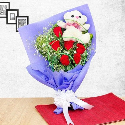Bouquet of red roses with white teddy bear wrapped in purple paper, ideal for gifting