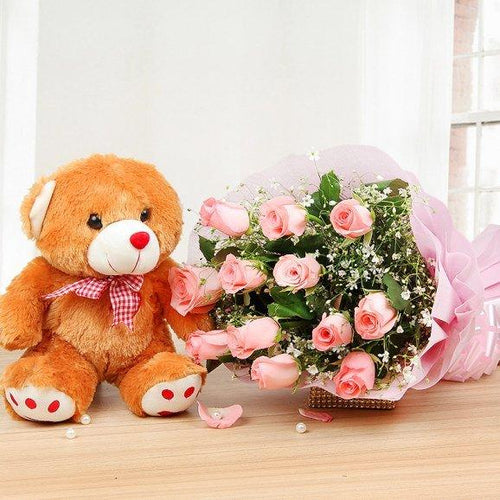 Brown teddy bear with a pink bow tie next to a bouquet of pink roses 