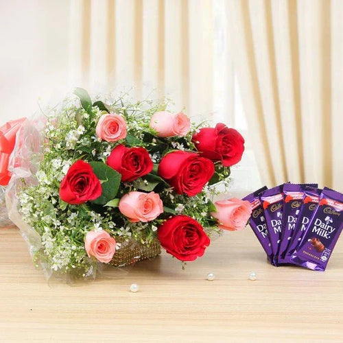 Bouquet of red and pink roses with Cadbury Dairy Milk chocolate bars on a wooden surface.