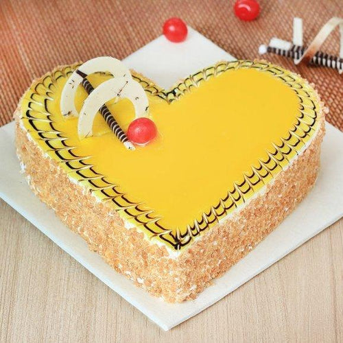 Heart-shaped cake with yellow frosting and decorative elements on a wooden surface