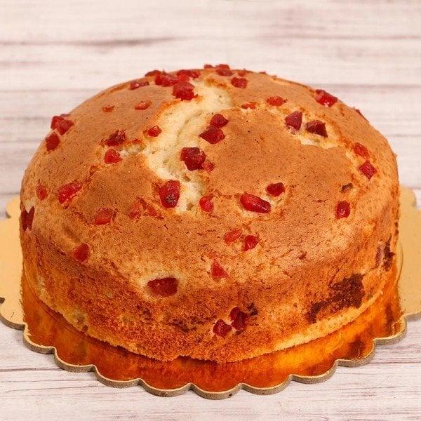 Round cake with red fruit pieces on a wooden surface