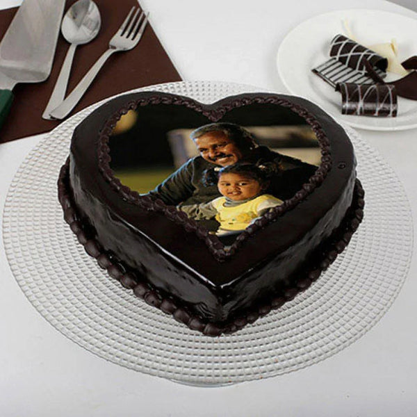 Heart-shaped chocolate cake with a photo of a man and a child on a white table.