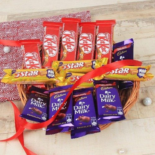 Basket filled with various chocolate bars including KitKat, 5 Star, and Cadbury Dairy Milk on a wooden surface.