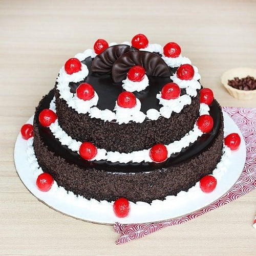 Two-tiered chocolate cake with red cherries on a light wooden background