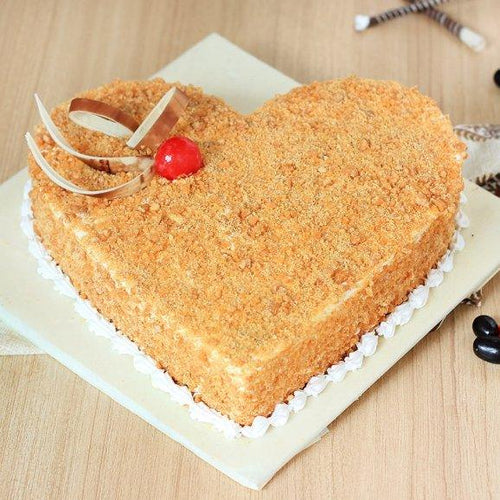 Heart-shaped cake with a cherry and ribbon on a wooden surface