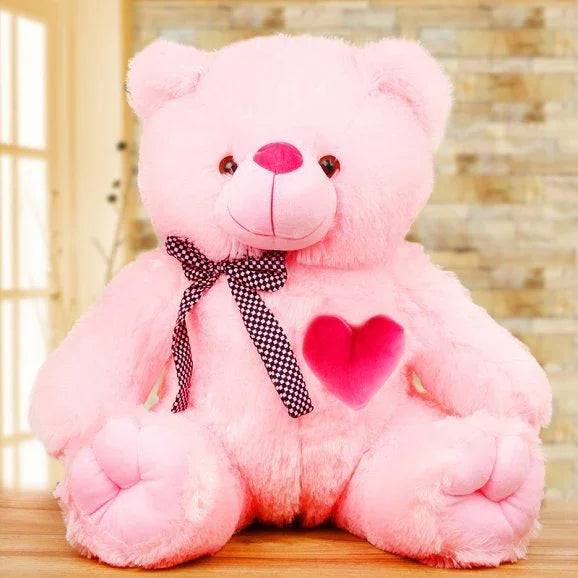 Pink teddy bear with a heart and bow tie on a wooden surface.