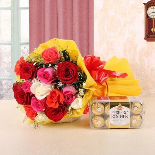 Bouquet of red, pink, and white roses with a box of Ferrero Rocher chocolates on a light surface.