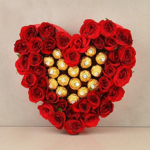 Heart-shaped arrangement of red roses with gold Ferrero Rocher chocolates on a beige background