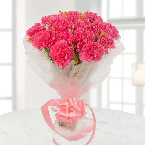 Bouquet of pink flowers wrapped in white paper with a pink bow on a white surface.