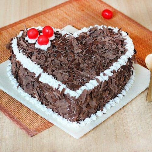 Heart-shaped chocolate cake with white frosting and red cherries on a wooden board.