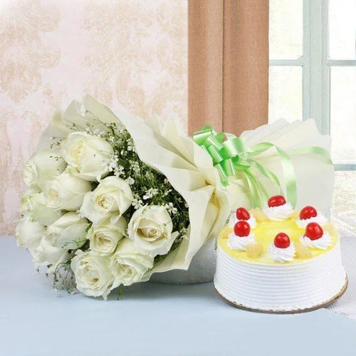 Bouquet of white roses and a small cake with red berries on a light surface.